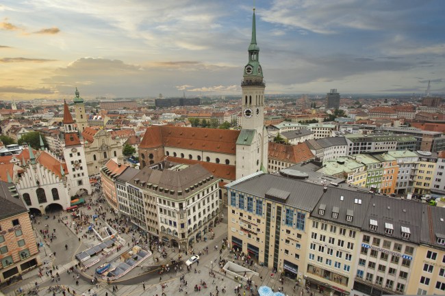 Luftbild über München mit Blick auf die Altstadt rund um den Marienplatz, die Pfarrkirche St. Peter, deren markanter Turm sowie das Alte Rathaus mit seinem spitzen roten Turmdach.