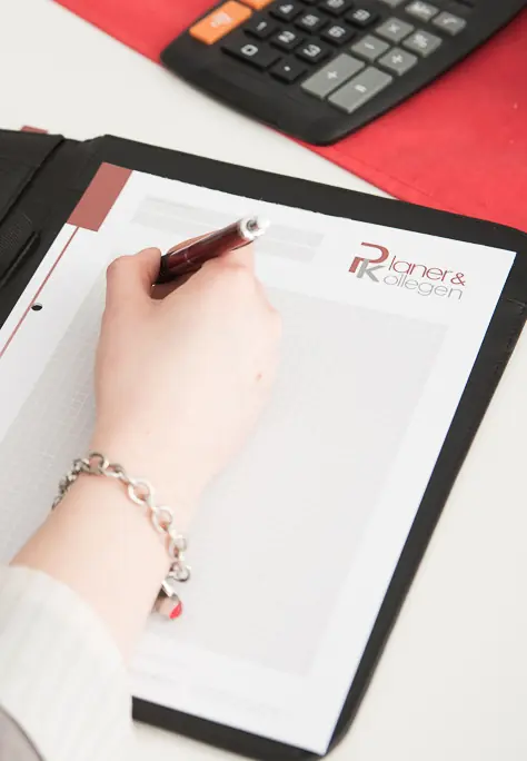 Block mit Planer & Kollegen Logo und eine Hand mit Stift, die Notizen aufnimmt